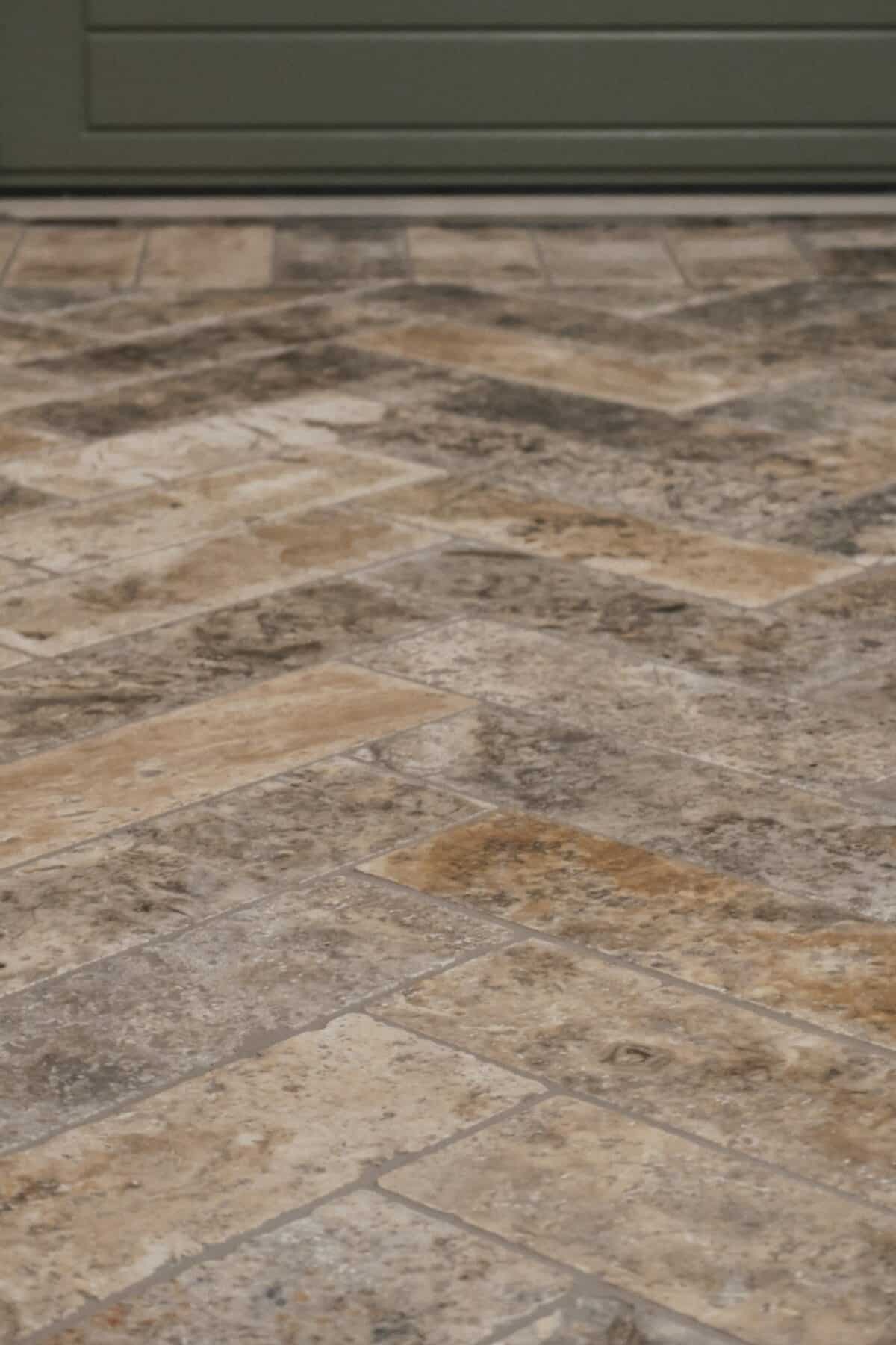 Podłoga z trawertynu ASH MIX cegiełka bębnowana 30,5x10x1 cm przy wejściu, harmonizująca z zielonymi drzwiami i rustykalnym wystrojem wnętrza.
