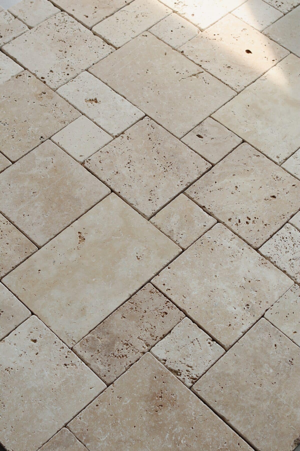 Podłoga z trawertynu IVORY MIX MINI w układzie rzymskim, złożona z płytek w ciepłych beżowych tonacjach z widocznymi porami i naturalnymi przebarwieniami. Światło podkreśla fakturę kamienia, nadając przestrzeni przytulny charakter.