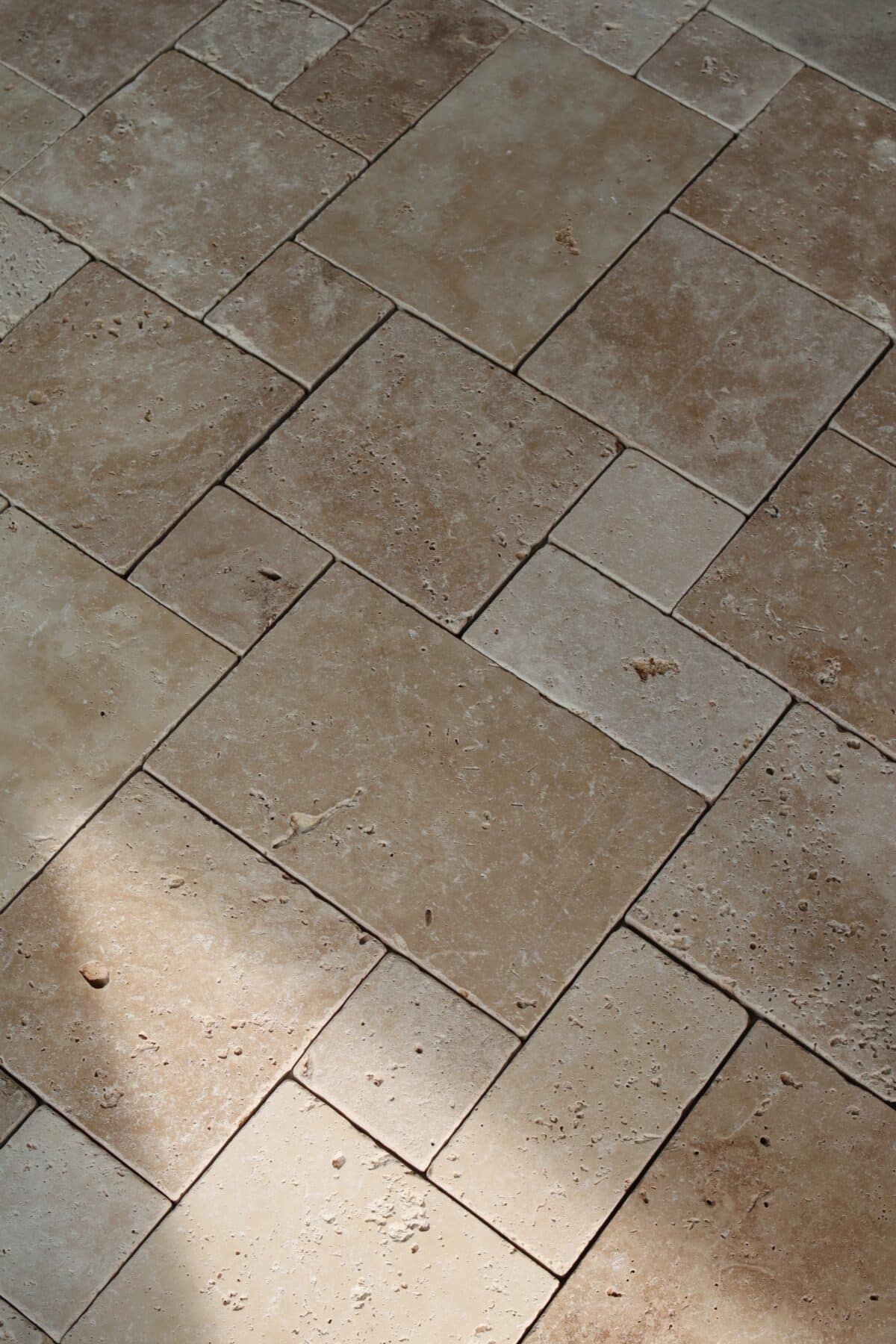 Podłoga z trawertynu IVORY MIX MINI w układzie rzymskim, składająca się z płytek w różnych rozmiarach w ciepłych beżowych odcieniach. Widoczne naturalne pory i delikatne przebarwienia nadają powierzchni autentyczny, elegancki wygląd.