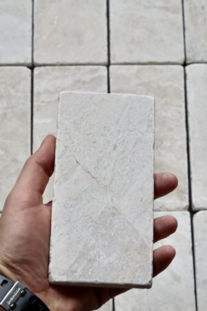 Marmurowa cegiełka Queen Beige o wymiarach 15x7,5 cm w szlifowanym wykończeniu, prezentowana w dłoni na tle ułożonych płytek.