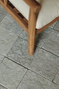 Kamienne płytki TANDUR GREY 20x20 cm z półszlifem i bębnowanymi krawędziami, widoczne obok fotela z jasną poduszką