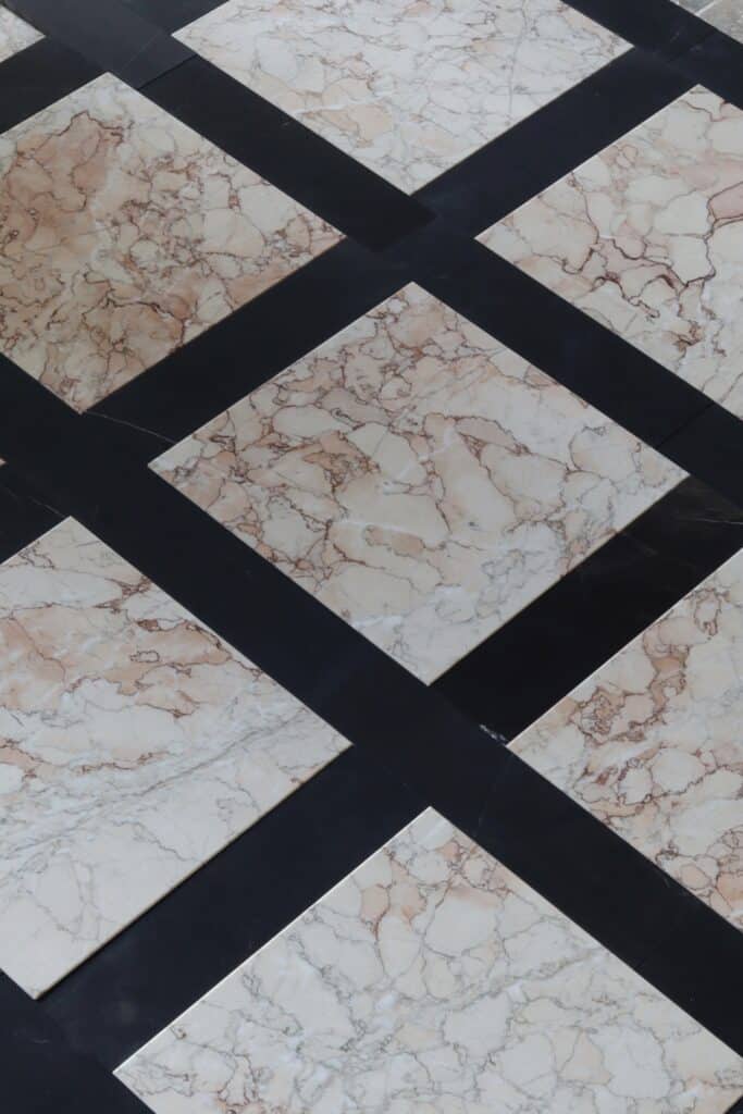 Podłoga z marmuru Sakura w formacie 30,5x30,5 cm, ułożona z czarnymi pasami w stylu szachownicy – jasne płytki z różowo-brązowym żyłkowaniem na tle czerni.